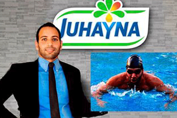 A man sits in a wheelchair in front of images of a Juhayna logo and photo of himself swimming