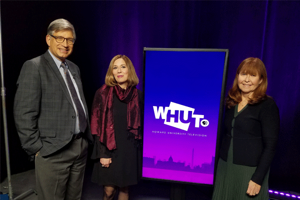 A man and two women stand on either side of a WHUT Tv sign.