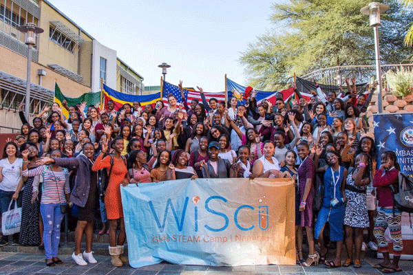 A large group of teenage girls hold a banner that says WiSci