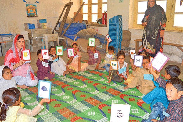 Children sit in a circle on the floor of a classroom holding up cards