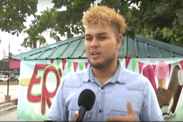 A young man speaks into a microphone for an interview outside.