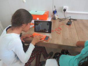 A girl types on a small orange keyboard while watching a small computer screen.