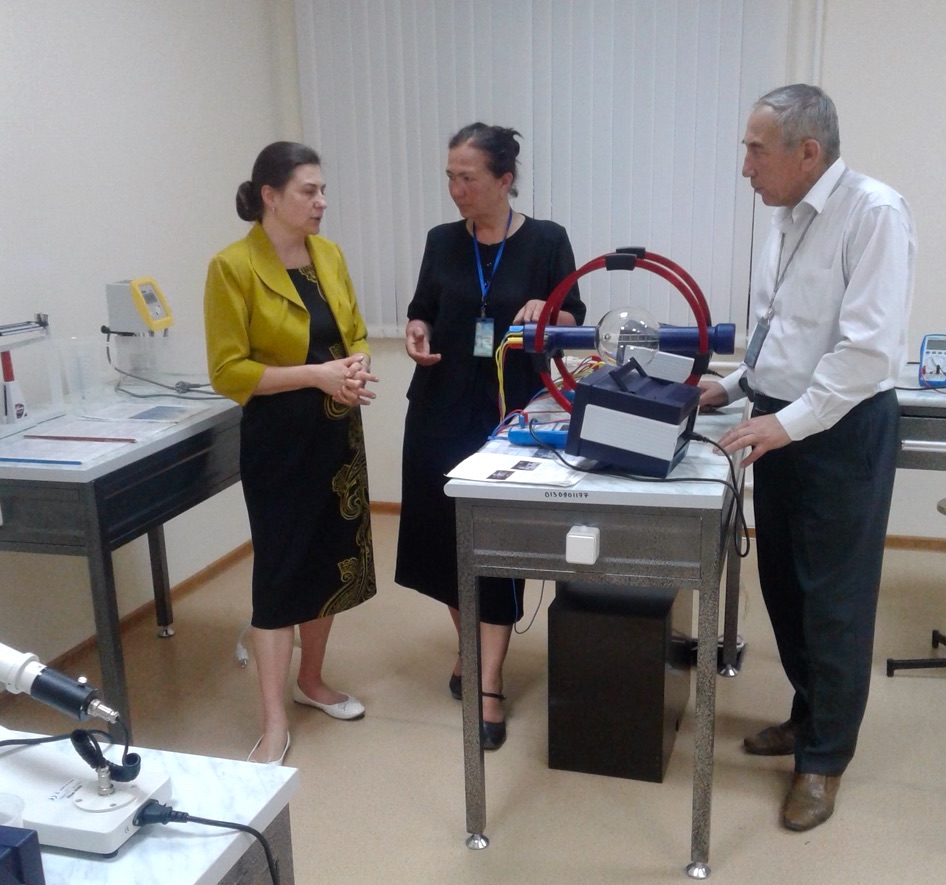 Two women and a man talk while standing next to lab equipment.