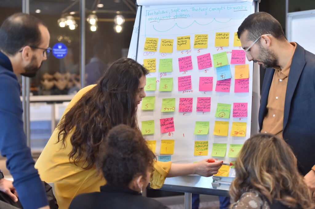 Five fellows discuss a waste management project on a large notepad with sticky notes.