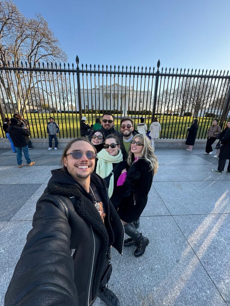 Six young adults pose for a selfie together in front of the White House in Washington, DC.