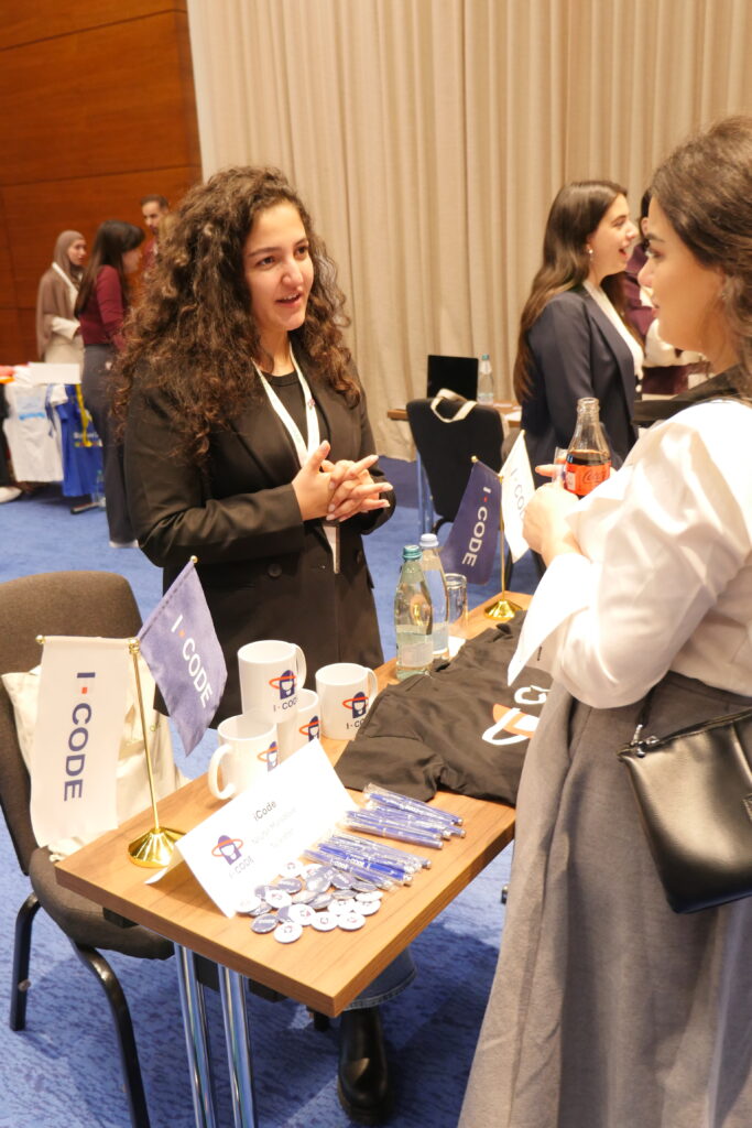 Two women at World Learning’s Global UGRAD seminar talk to each other across a table. The table has mugs, t-shirts, and pamphlets on it.
